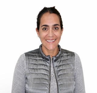 Portrait of a woman smiling at the camera wearing a gray quilted vest over a gray long-sleeve shirt
